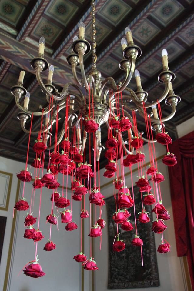 a chandelier with red roses hanging from it's sides in a room