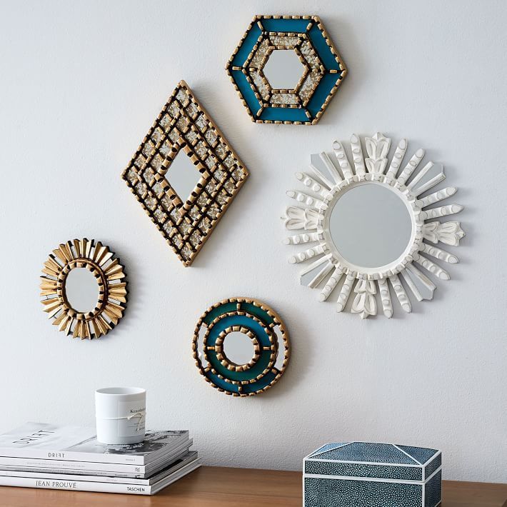 four decorative mirrors mounted on the wall above a wooden table with a cup and stack of books