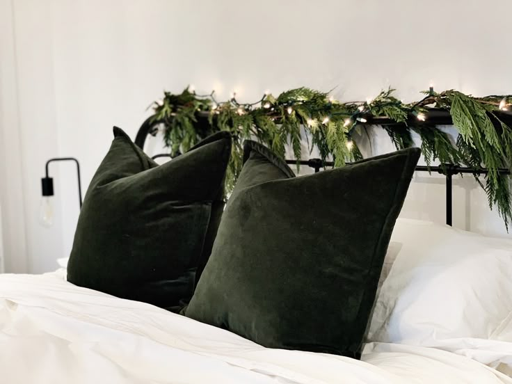 two green pillows sitting on top of a bed next to a white comforter covered in christmas greenery