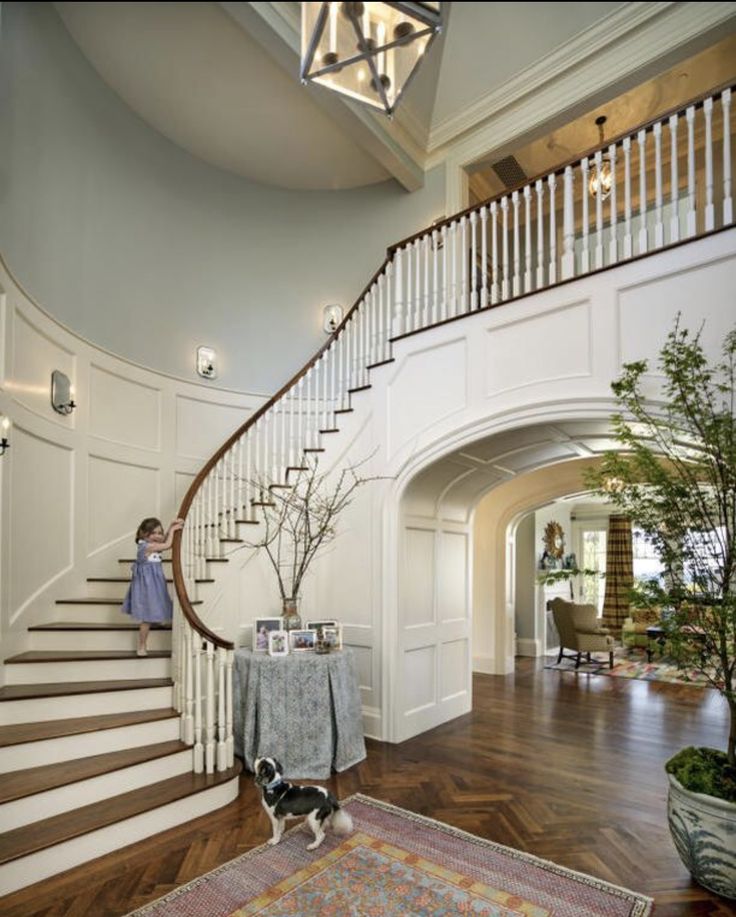 a woman standing on the stairs in a house with hardwood flooring and white walls