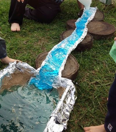 a person standing in the grass next to a small stream made out of tin foil