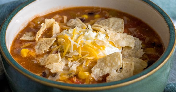 a bowl of soup with tortilla chips and sour cream on top, ready to be eaten