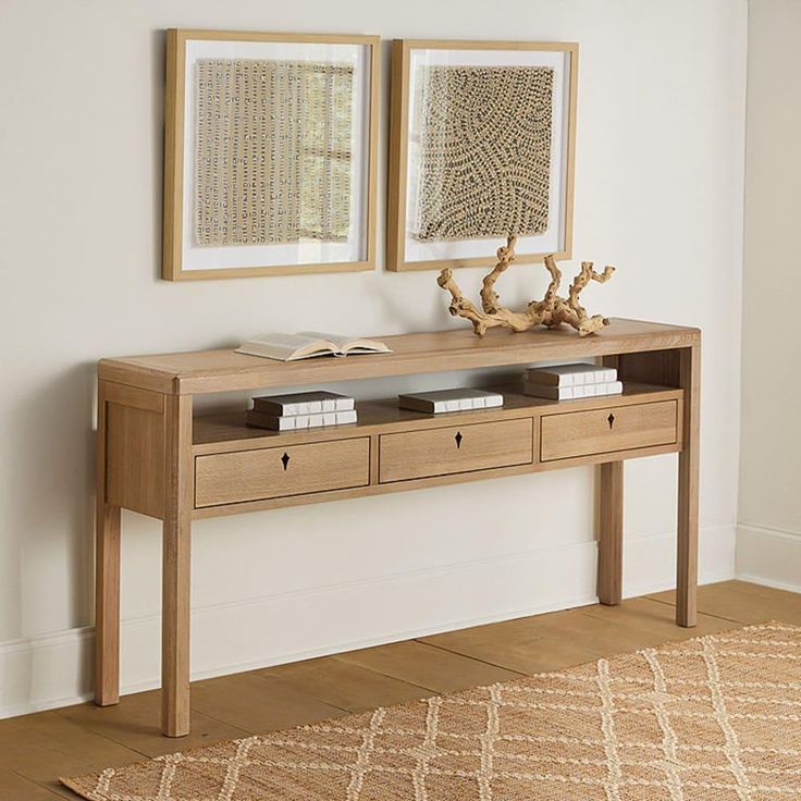 two framed pictures hang on the wall above a wooden console table with drawers and books