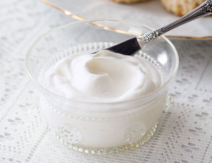 a glass bowl filled with whipped cream on top of a table next to some cookies