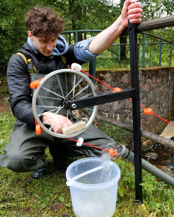 a man is working on a bicycle wheel in the grass near a bucket and fence