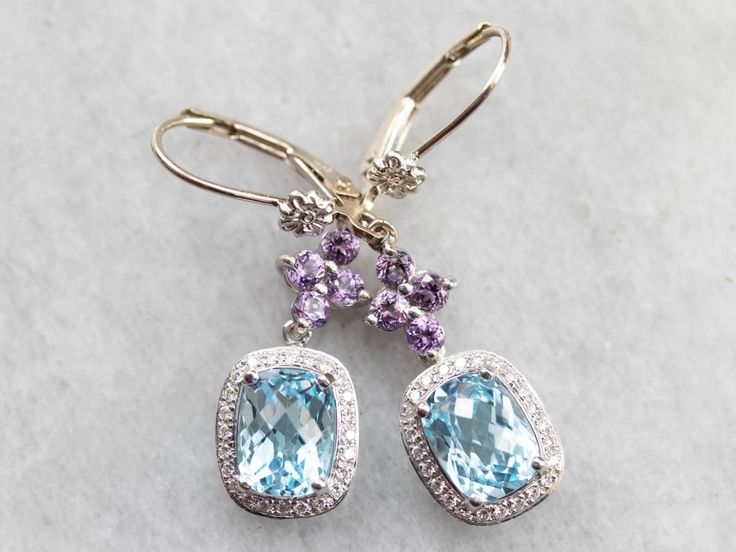 Easily transition from bridal to everyday wear with style in these lovely drop earrings! We've set amethyst floral drops with glittering diamond halos set with heavenly blue topaz gemstones, making a one of a kind pair of earrings that are the perfect gift for the bride to be! Metal: 14K White Gold, 18K White Gold Gem: 2 Blue Topaz Gem Measurements: 6.2 x 8.0 mm, Rectangle Cushion Cut Accents: 8 Amethyst, 48 Diamonds totaling .24 Carats, G in Color, VS in Clarity Earrings Length: 37 mm Earrings Gold Earrings Bridal, Rectangle Cushion, Gift For The Bride, Halo Setting, Diamond Glitter, White Gold Earrings, Diamond Drops, Bride To Be, Topaz Gemstone