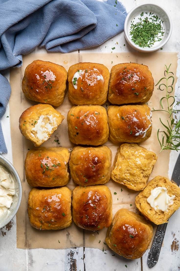 small rolls with cheese and herbs on a piece of parchment paper next to a bowl of dip