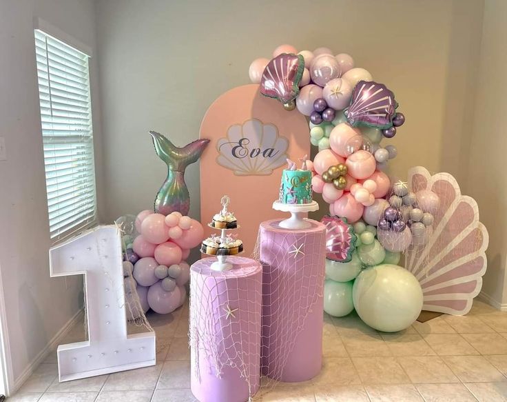 a table with balloons, mermaid decorations and other items for a first birthday party or baby shower