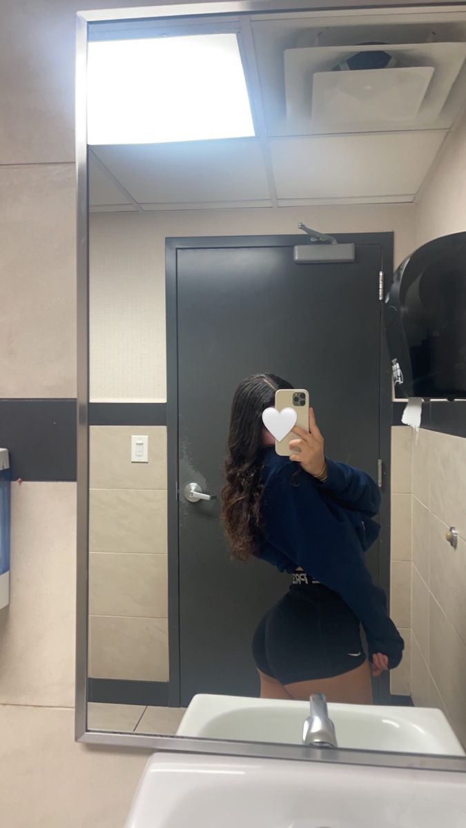 a woman taking a selfie in front of a bathroom mirror with her cell phone