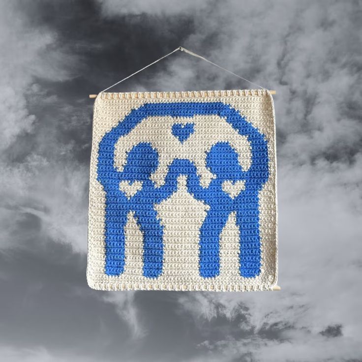 a blue and white crocheted sign hanging from a string on a cloudy sky