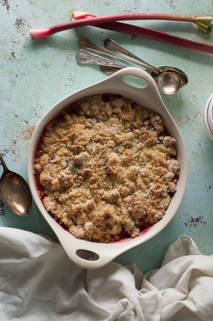 a baked dish with crumbs and spoons next to it on a blue surface