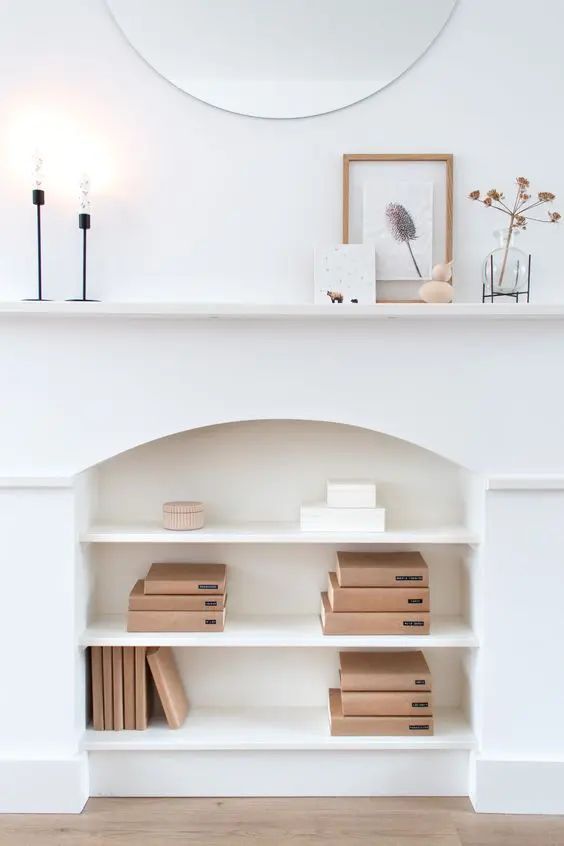 there is a white shelf with books on it and a mirror above the bookcase