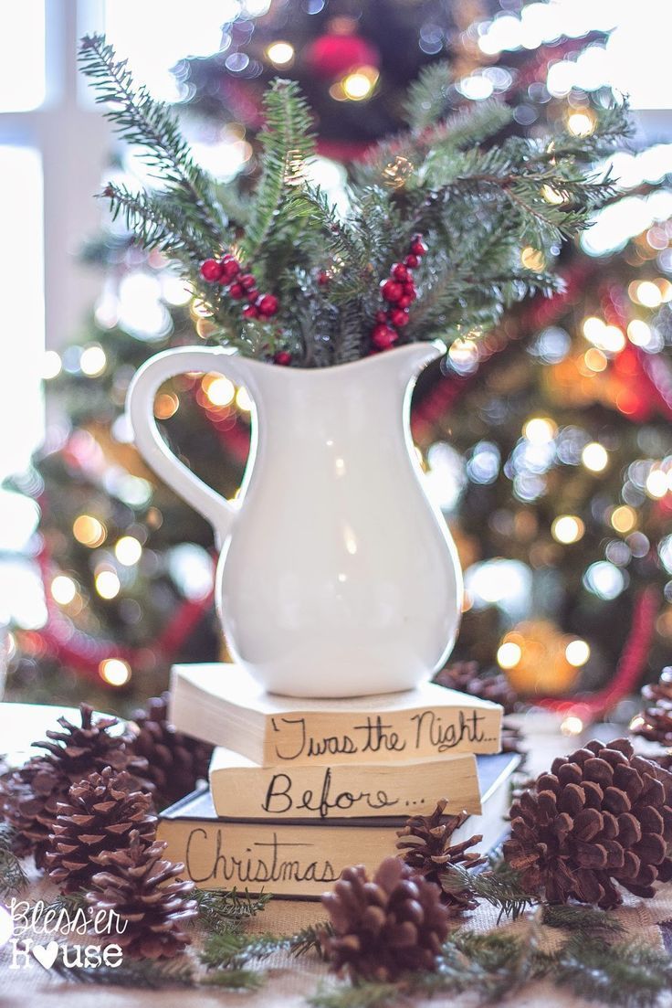 a white pitcher sitting on top of two books next to a christmas tree with pine cones