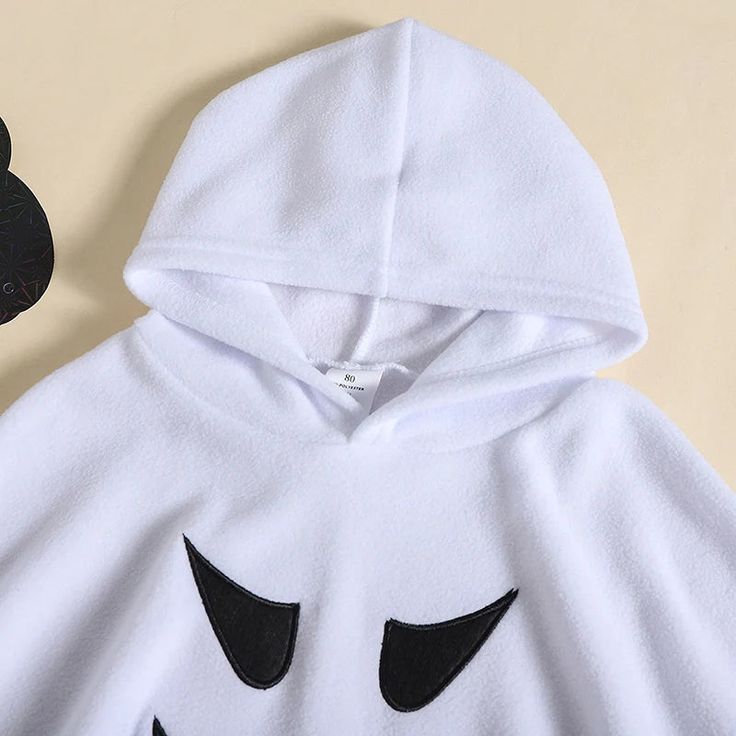 a white hooded sweatshirt with black eyes and ears on the hood, next to a pair of scissors