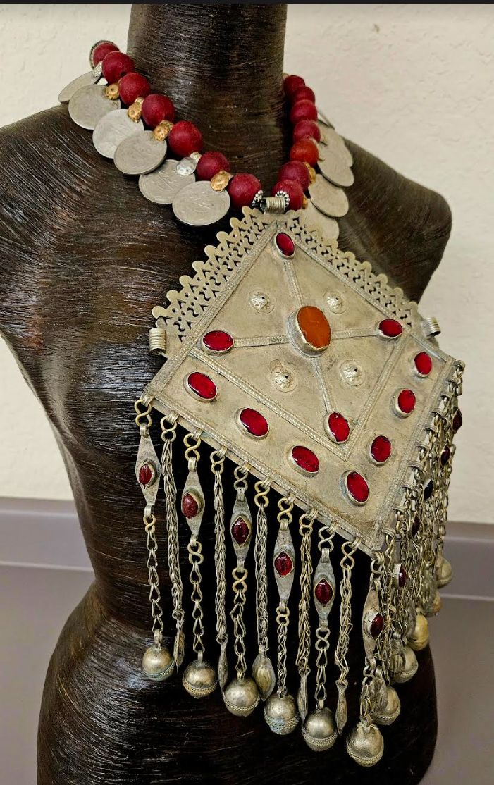 Here's another piece from my private vault. A huge Kuchi, Turkman or Waziri inlaid red glass and mixed alloy metal breastplate pendant is the focal point on this one-of-a-kind ethnic masterpiece with 21 intact dangles with attached bells. The pendant portion measures 12" x 7" and features inlaid red glass which is purposefully used to ward off the "evil eye. I suspended this from a red glass recycled African beaded and vintage Kuchi coin necklace which adjusts from 17-20". Has an inlaid Kuchi coin suspended off the extender chain. Silver tone hardware with a medium sized lobster claw clasp. 3" extender chain. From the Atelier of Kat Kouture. Metal Breastplate, Indigenous Futurism, Photoshoot Jewelry, Rocker Chic Accessories, Kuchi Jewelry, Afghan Fashion, Unique Pendant Necklace, Statement Bib Necklace, Advanced Style