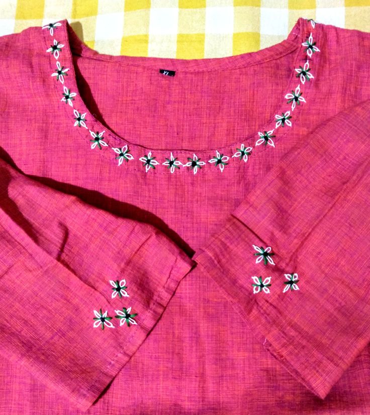 a pink shirt with white flowers on the chest and collar, sitting on a yellow checkered tablecloth