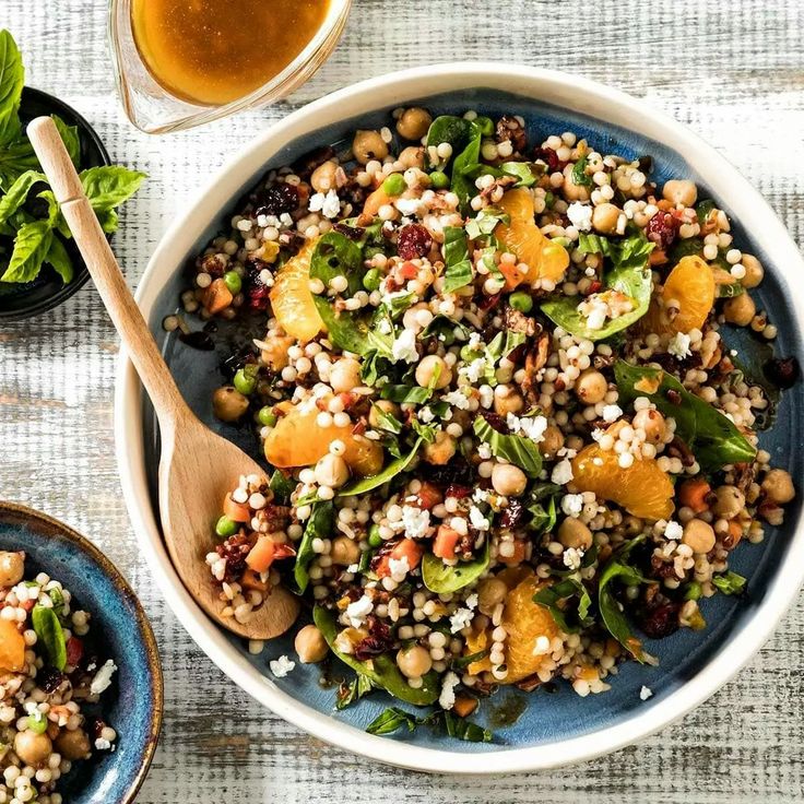 a bowl filled with grains and vegetables next to two bowls full of greens, oranges, and tea