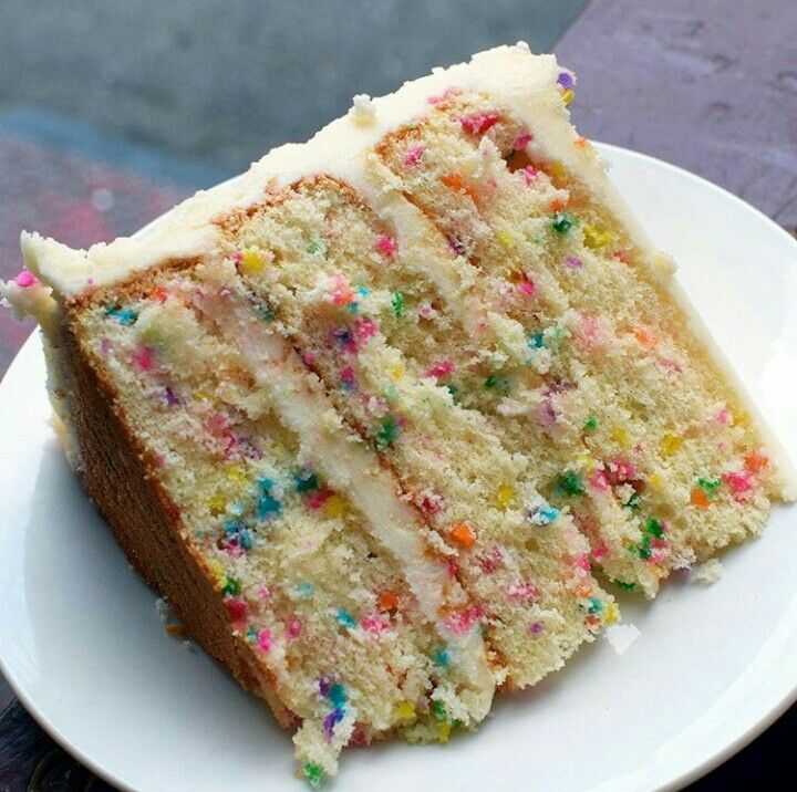 a slice of cake with white frosting and sprinkles on a plate