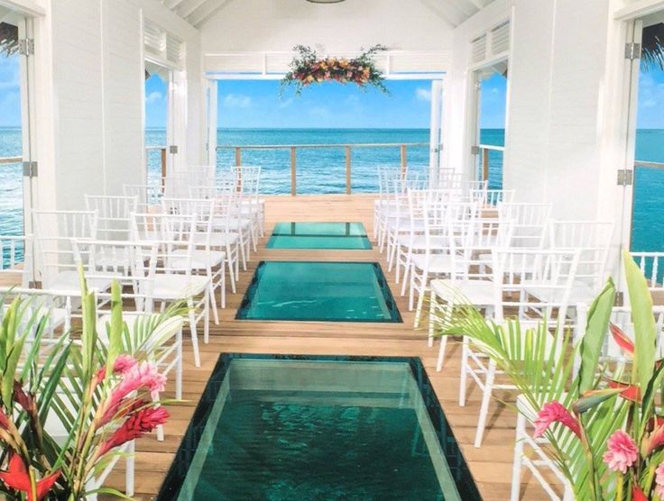 an indoor wedding venue overlooking the ocean with white chairs and floral arrangements on either side