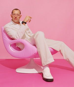 a man sitting in a pink chair with one foot on the ground and pointing at something