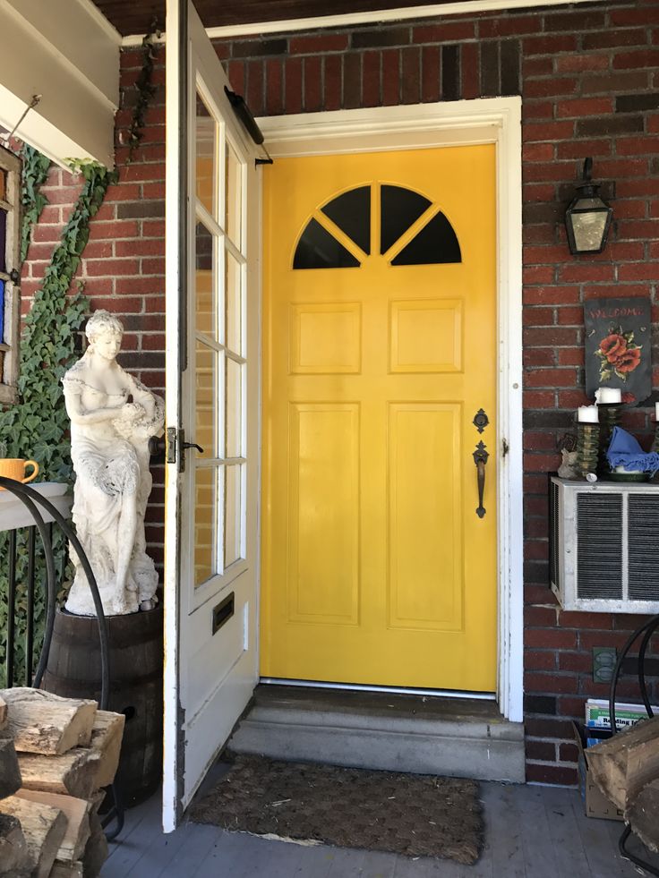 a yellow front door with a statue on the porch next to it and a black iron fence