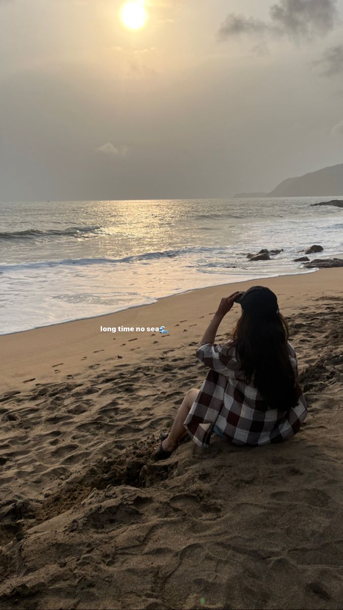 a woman sitting on top of a sandy beach next to the ocean