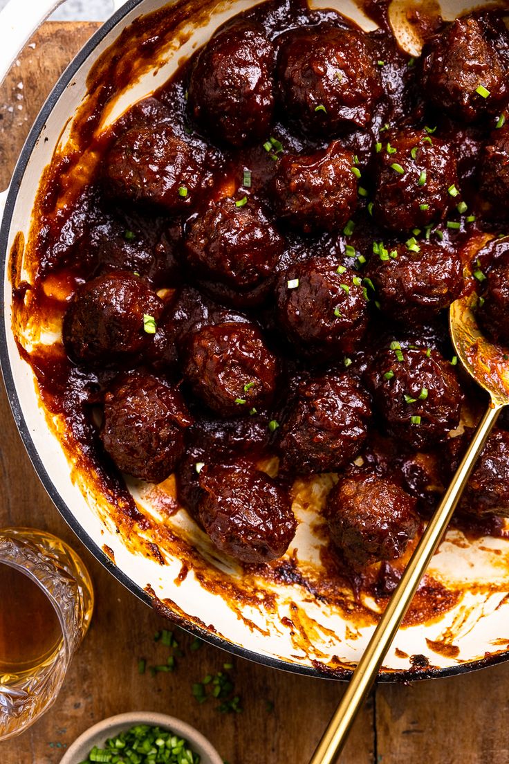 meatballs with sauce and green onions in a pan next to two glasses of beer