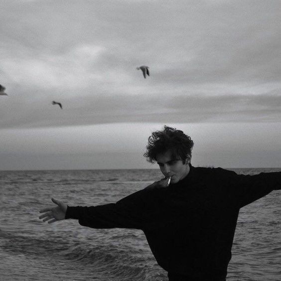 a man standing on top of a beach next to the ocean holding his arms out