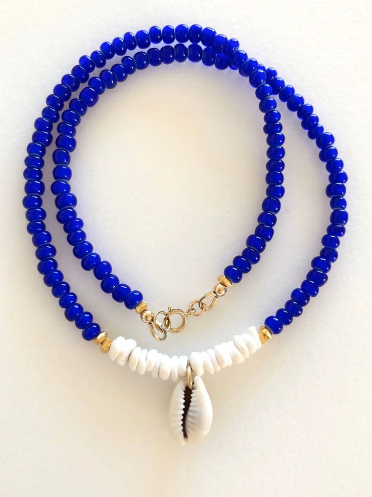 Beaded shell choker with cobalt blue African glass beads, Hawaiian white puka shells, genuine cowrie shell and Karen Hill Tribe 24k gold vermeil accents. Beaded summery necklace features vintage cobalt blue African white heart trade beads and genuine sea shells. Little white Hawaiian puka shells and genuine cowrie shell focal. Karen Hill Tribe 24k gold vermeil cube beads add fabulous accents. Beaded necklace closes with 14k gold fill spring ring clasp and findings. Blue Strand Shell Necklace For Vacation, Blue Polished Beads Jewelry For Beach, Blue Shell Necklace With Colorful Beads For Vacation, Blue Shell Necklace For Vacation, Blue Shell Beaded Necklaces With Round Beads, Blue Shell Necklace With Colorful Beads For Beach, Blue Beaded Shell Necklace For Beach, Vacation Blue Shell Necklace With Colorful Beads, Blue Shell Necklace For Beach