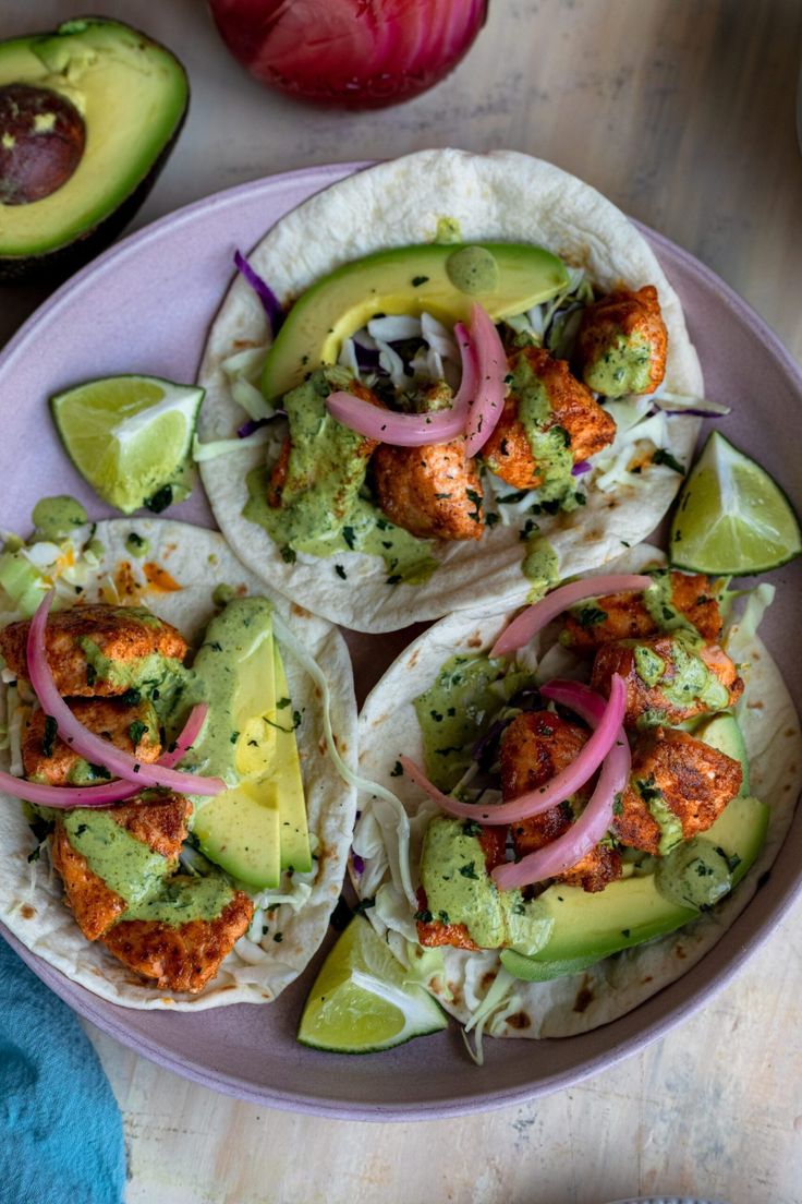 three fish tacos with avocado, onions and cilantro on a plate