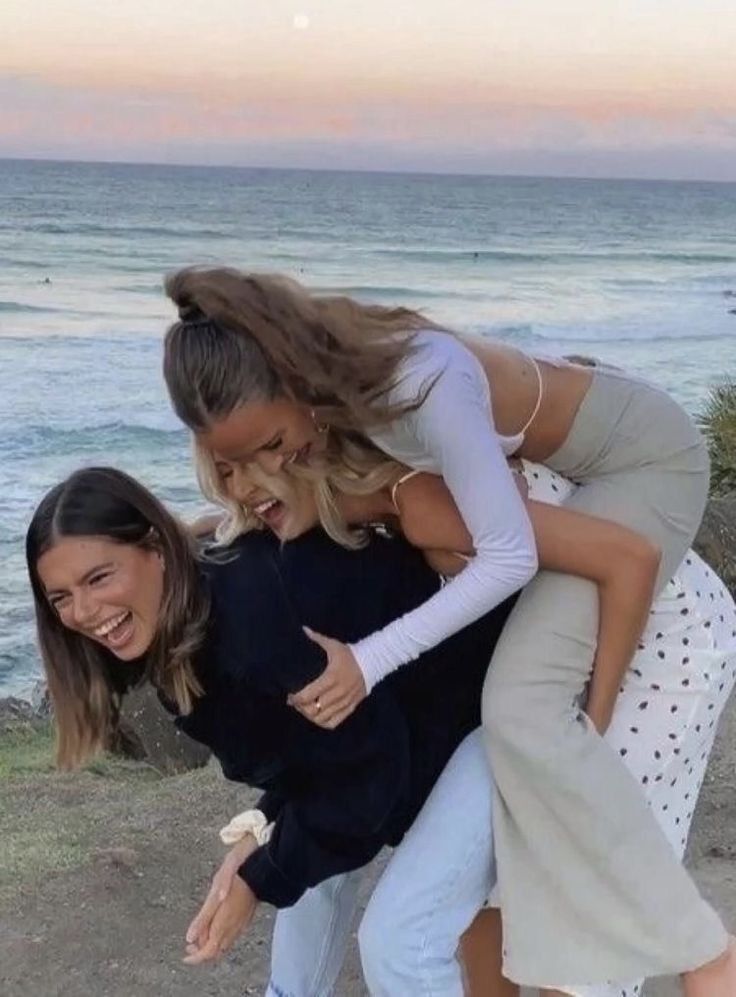 three women hugging each other while standing on the beach near the ocean with their arms around one another