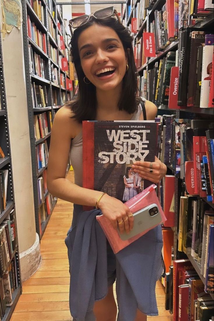 a woman is holding up a book in a bookstore aisle and smiling at the camera