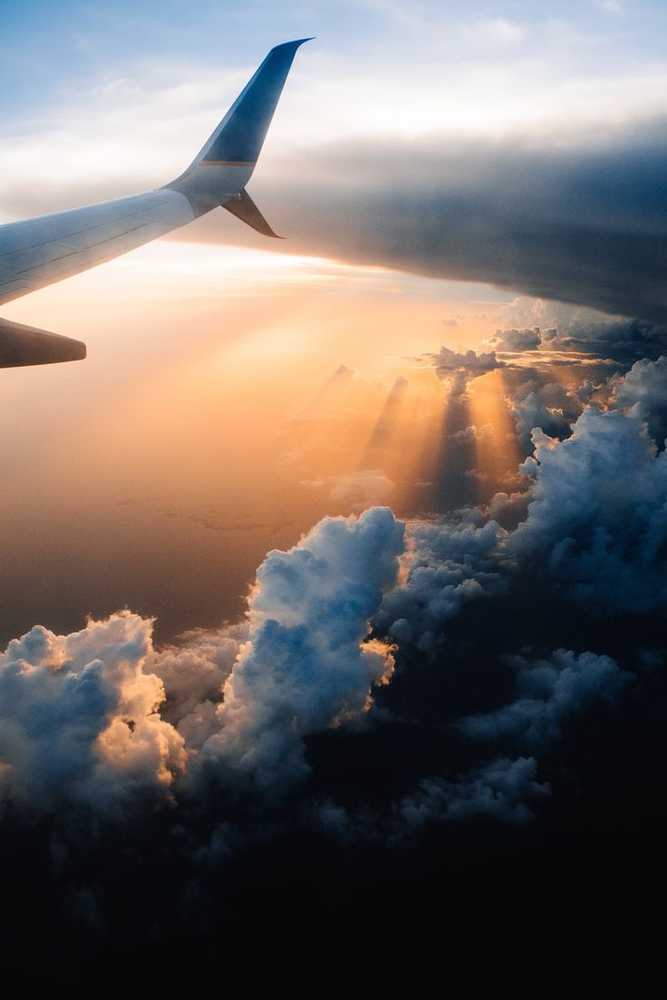 the wing of an airplane as it flies through the sky with clouds and sun rays