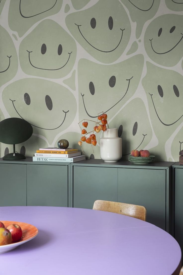 a purple table with fruit on it in front of a wallpapered wall and cabinet