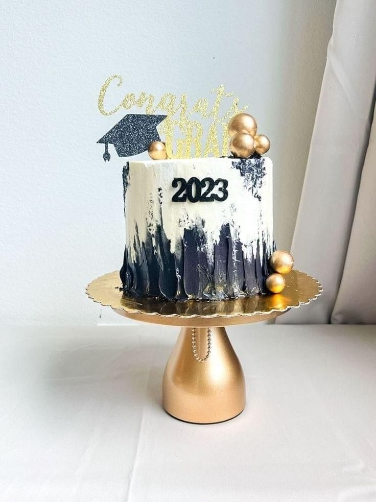 a white and gold graduation cake on top of a metal stand in front of a window