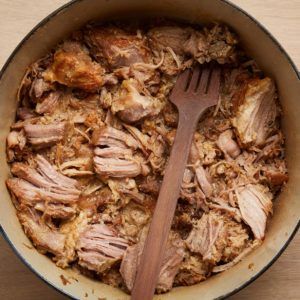 a pot filled with meat and potatoes on top of a wooden table next to a fork