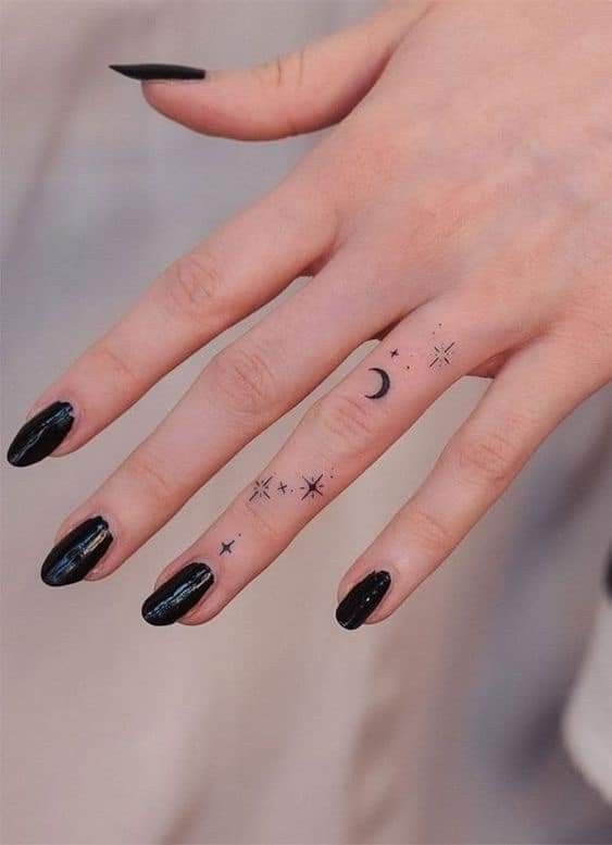 a woman's hand with black nail polish and stars on the ring finger tattoo