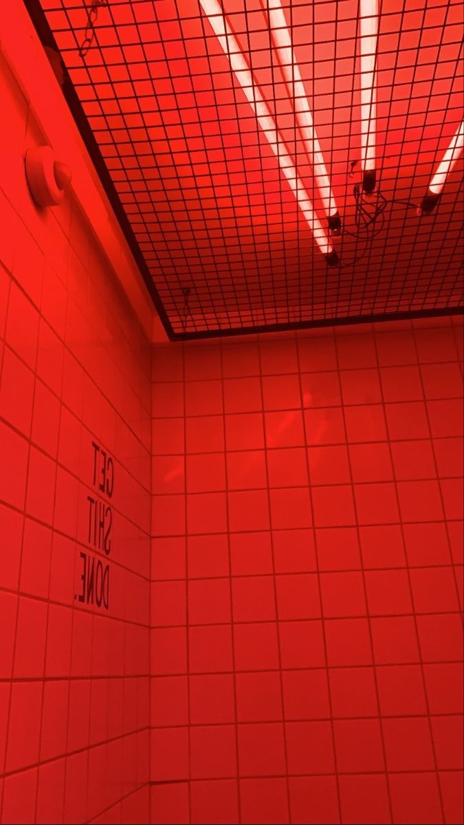 a bathroom with red light coming from the ceiling and tiled walls, along with white tile flooring