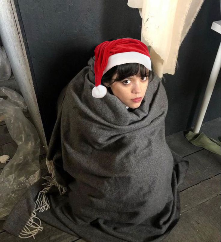 a woman wrapped up in a blanket with a santa hat on her head and looking at the camera