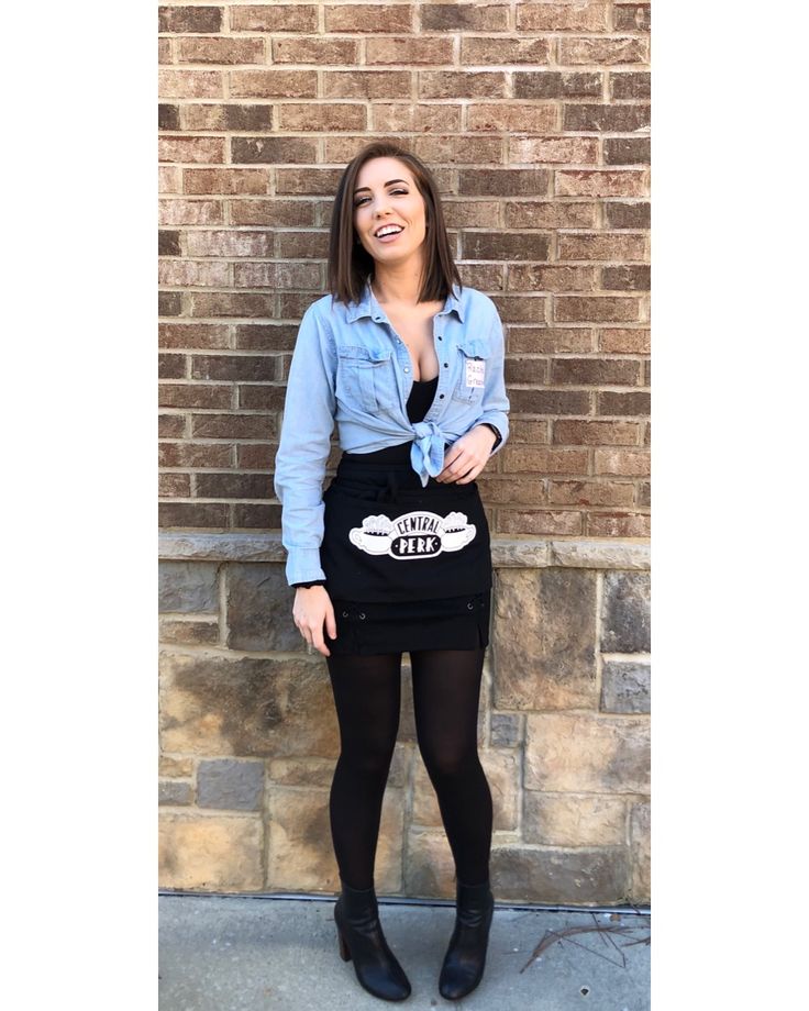 a woman standing in front of a brick wall wearing a denim shirt and black skirt