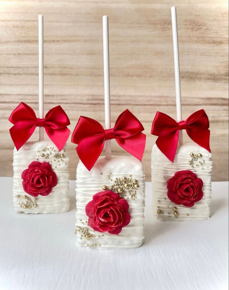 four small white vases with red roses and bows on them are sitting on a table