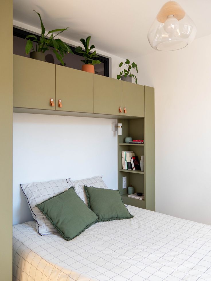 a bed with two green pillows on top of it next to a book shelf and potted plant