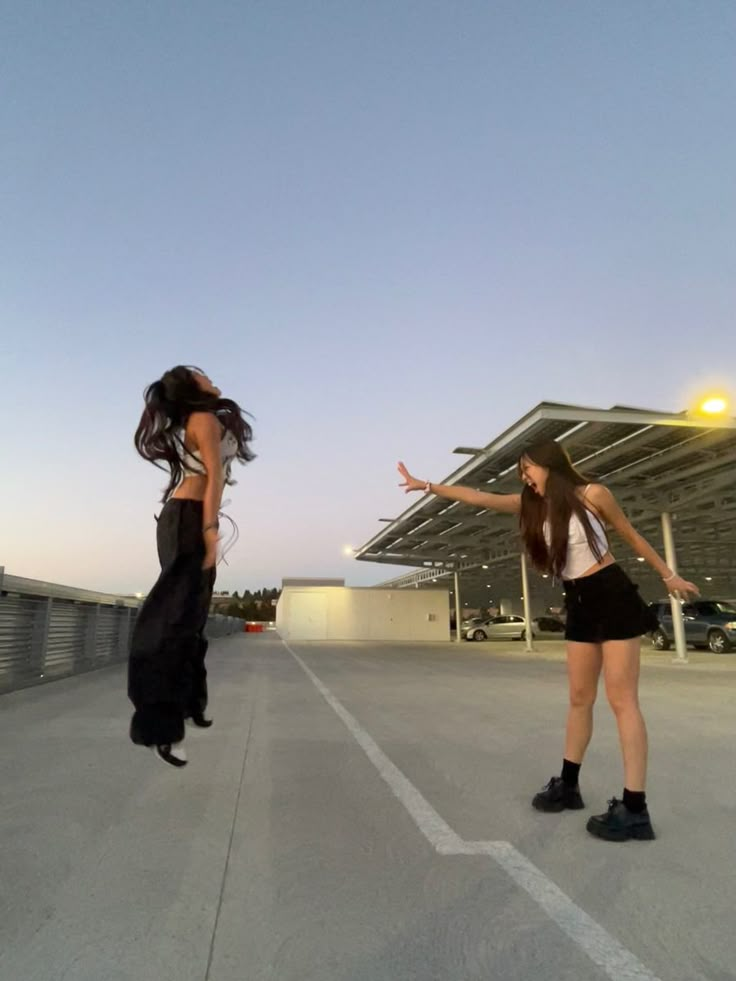 two girls are standing in an empty parking lot and one is holding out her hand