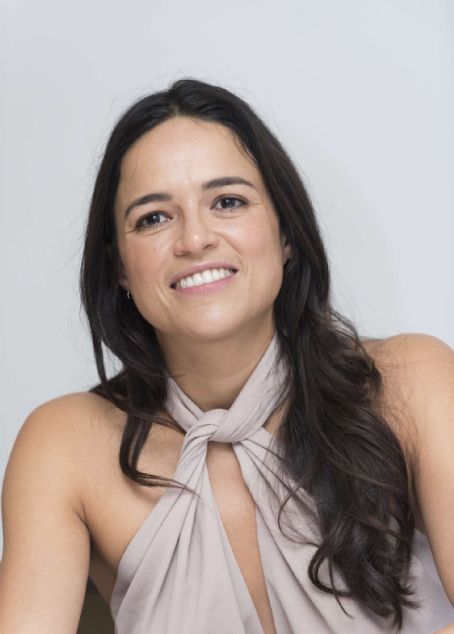 a woman with long hair wearing a halter top and smiling at the camera while sitting in front of a white background