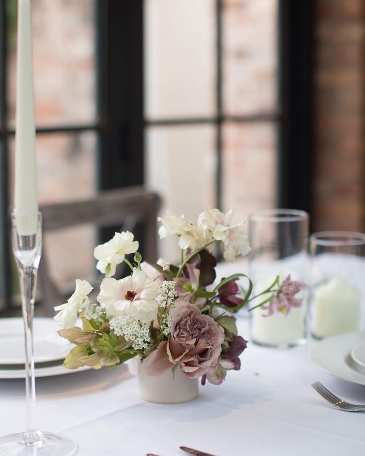 the table is set with white and purple flowers, silverware, candles and napkins