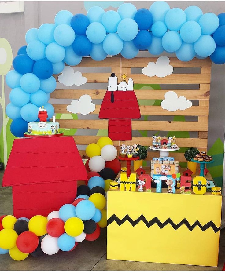 a birthday party with balloons and decorations on the table in front of a wooden fence