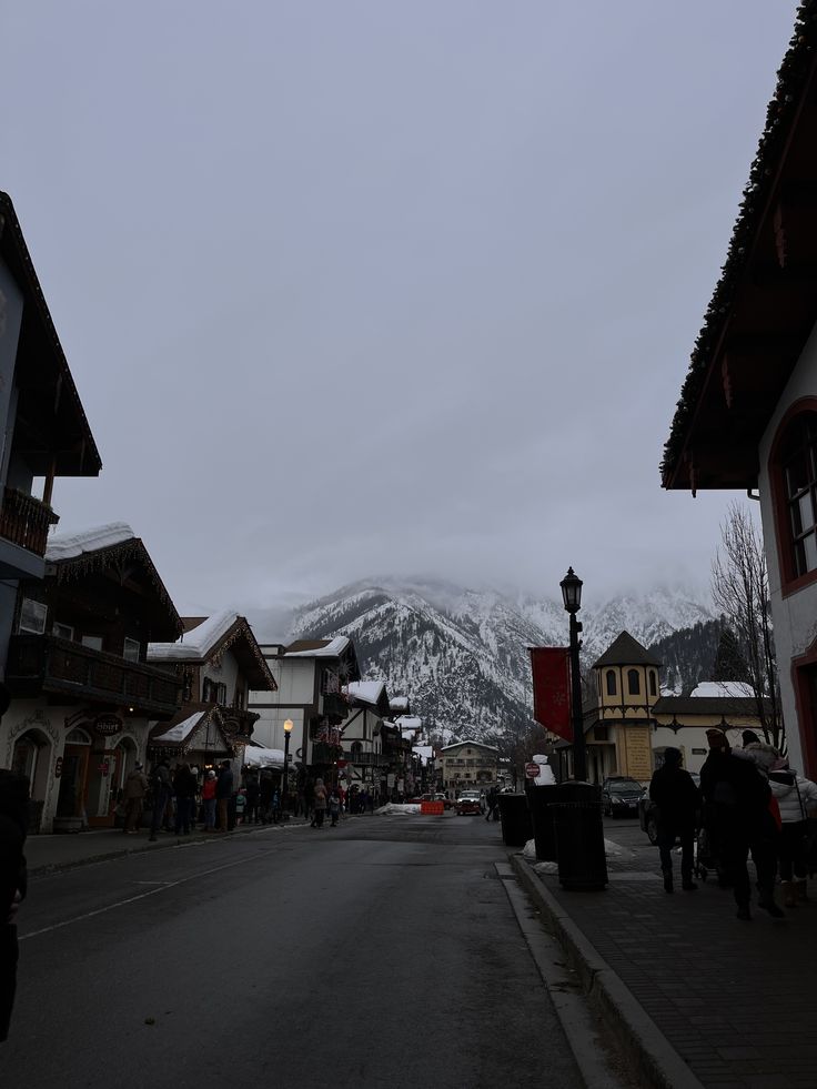 people are walking down the street in front of some buildings with mountains in the background