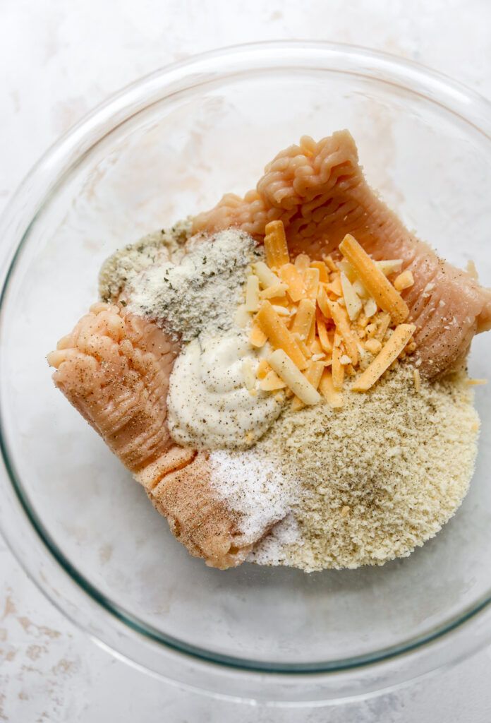 ingredients in a glass bowl on top of a white countertop, including breadcrumbs and cheese