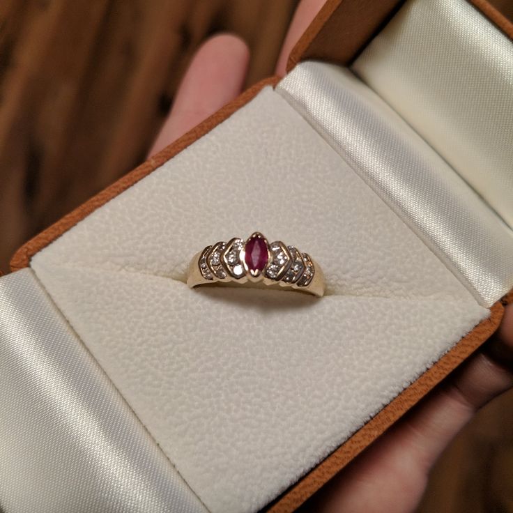 a woman's hand holding an engagement ring with two diamonds and a red stone