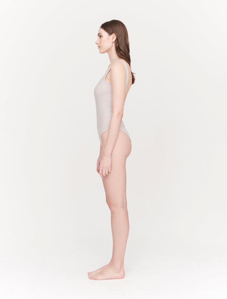 a woman in a white bodysuit is standing with her back turned to the camera